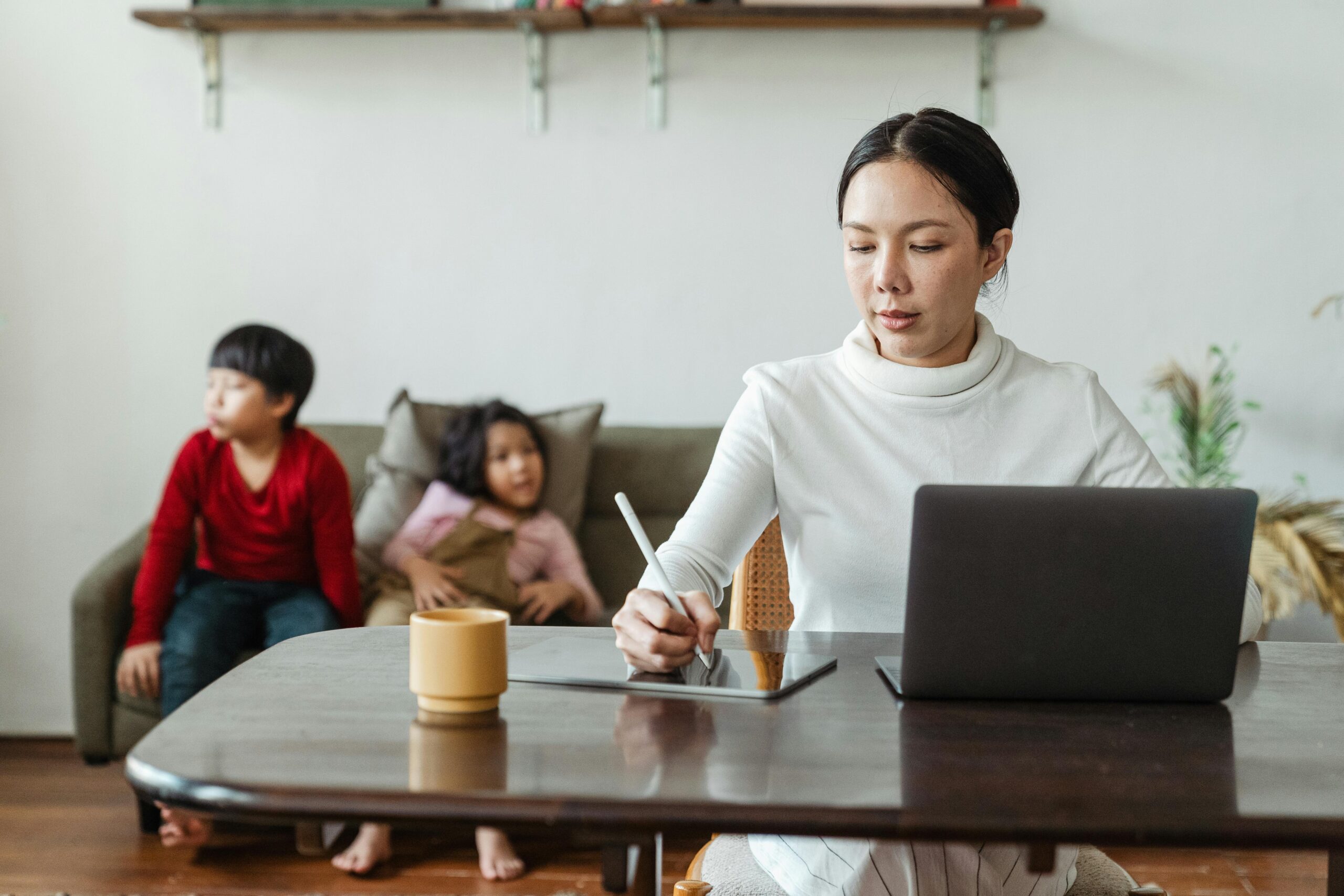 Asian mother balances remote work while supervising children at home.